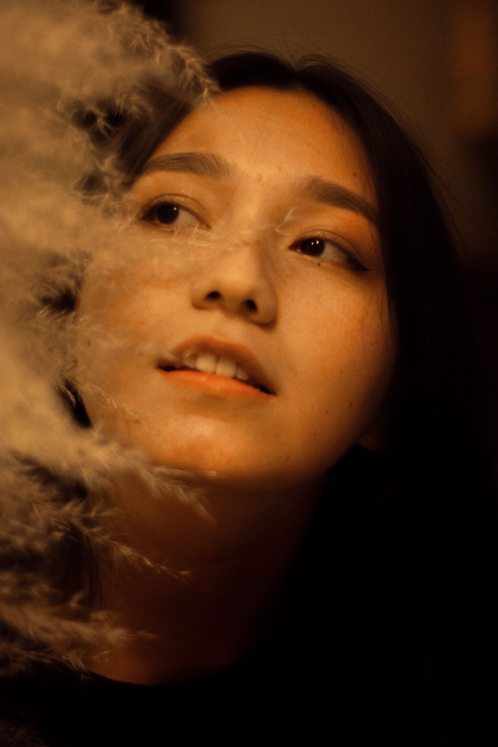 A dreamy portrait of a woman surrounded by soft, ethereal feathers indoors.