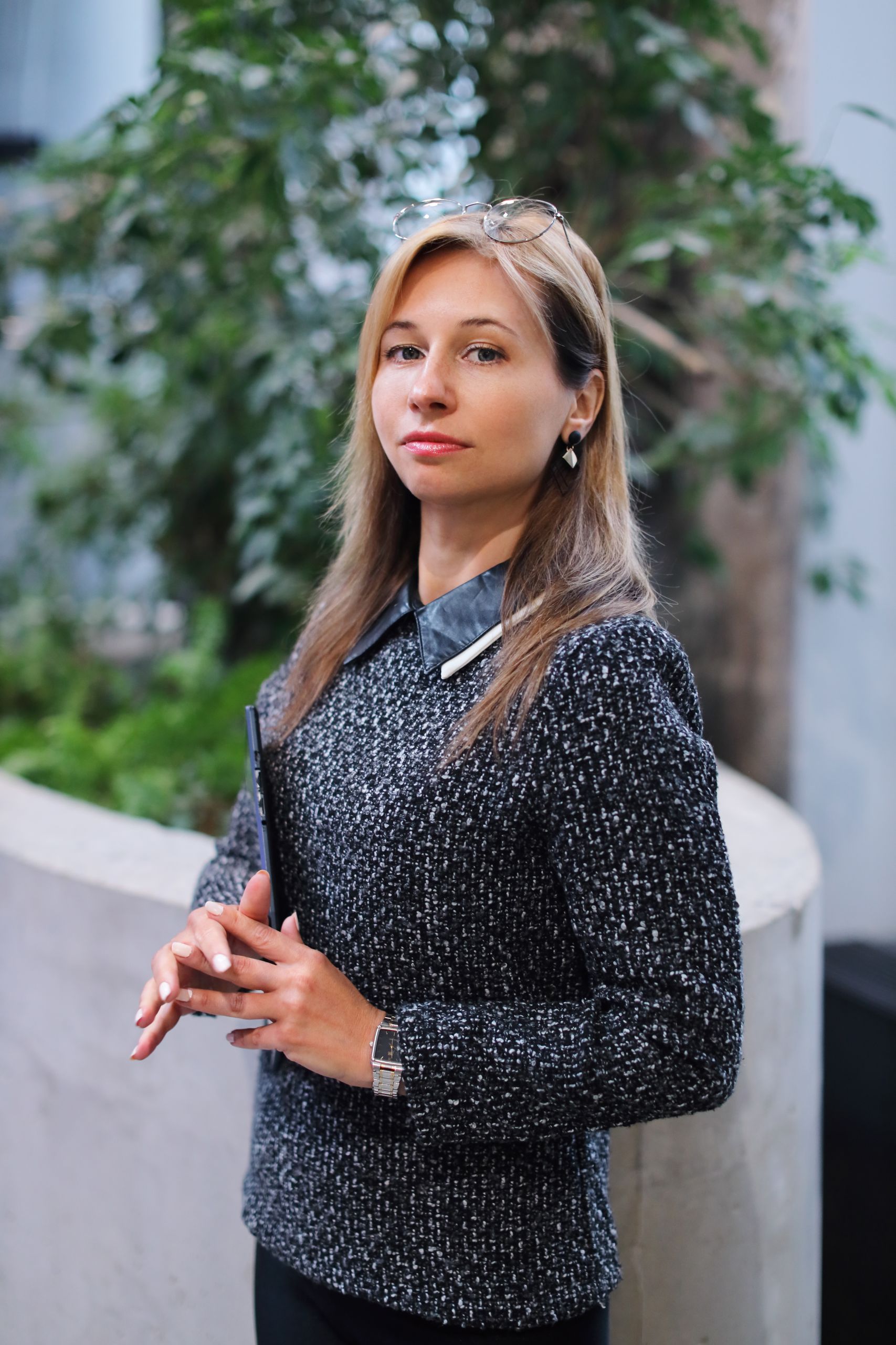 Confident woman in sweater with hands clasped, posing indoors in business setting.