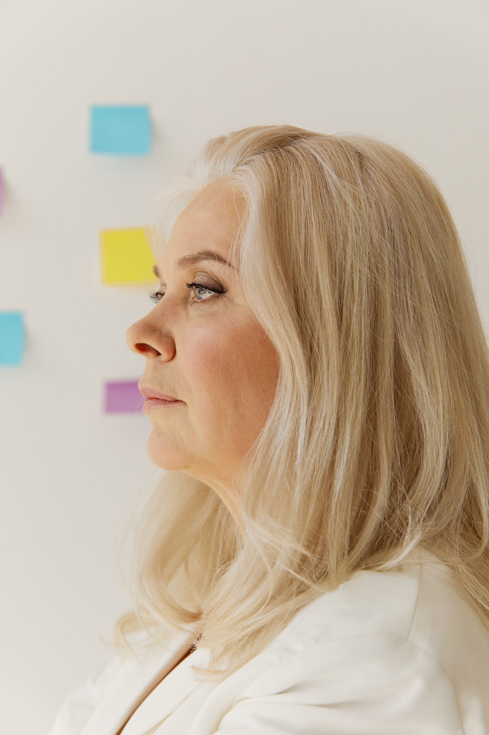 Side view of a blonde mature woman in an office setting with colorful sticky notes on a white wall.
